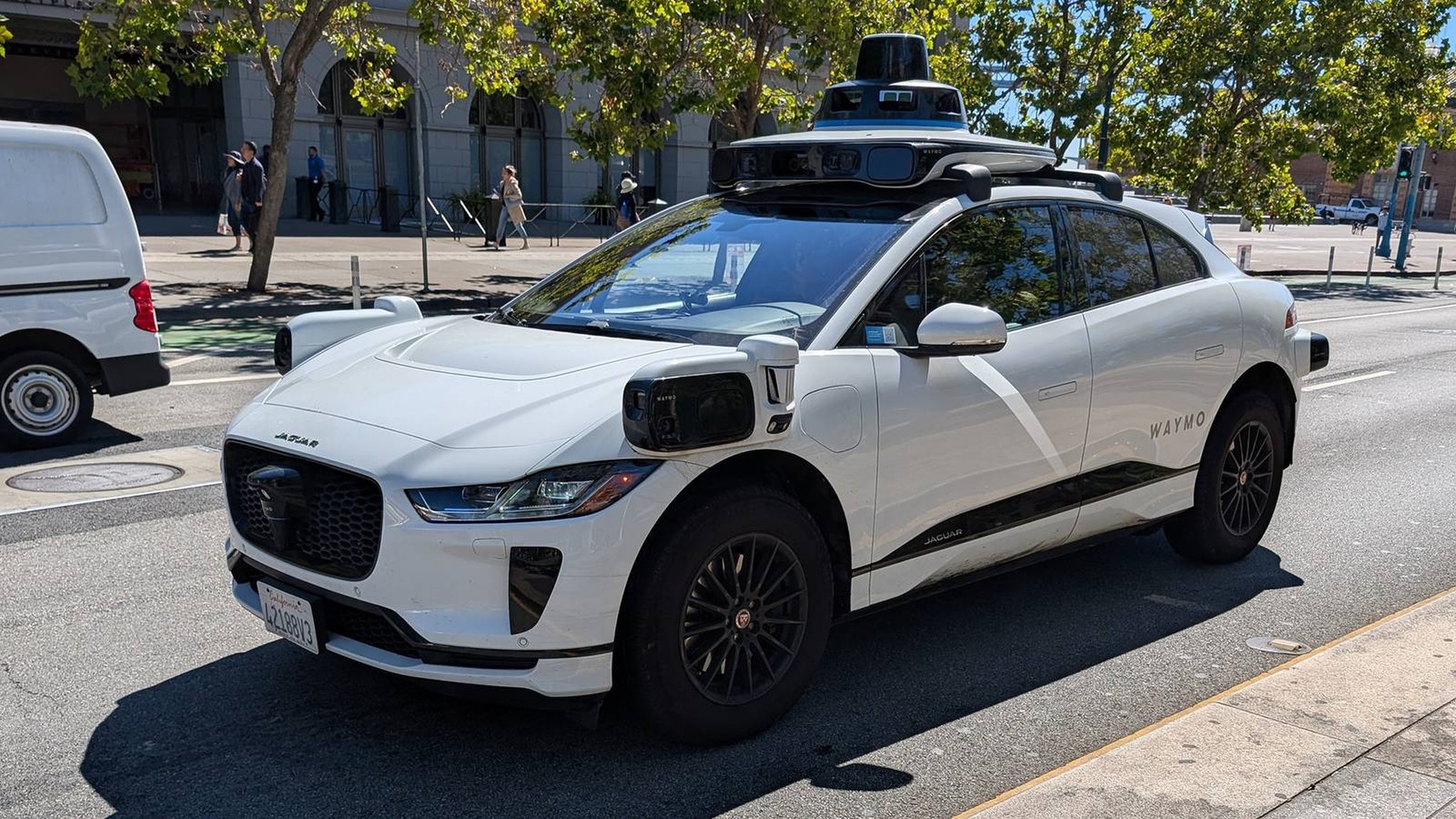 A white Waymo Jaguar I-Pace robotaxi with roof lidar stopped on a San Francisco street