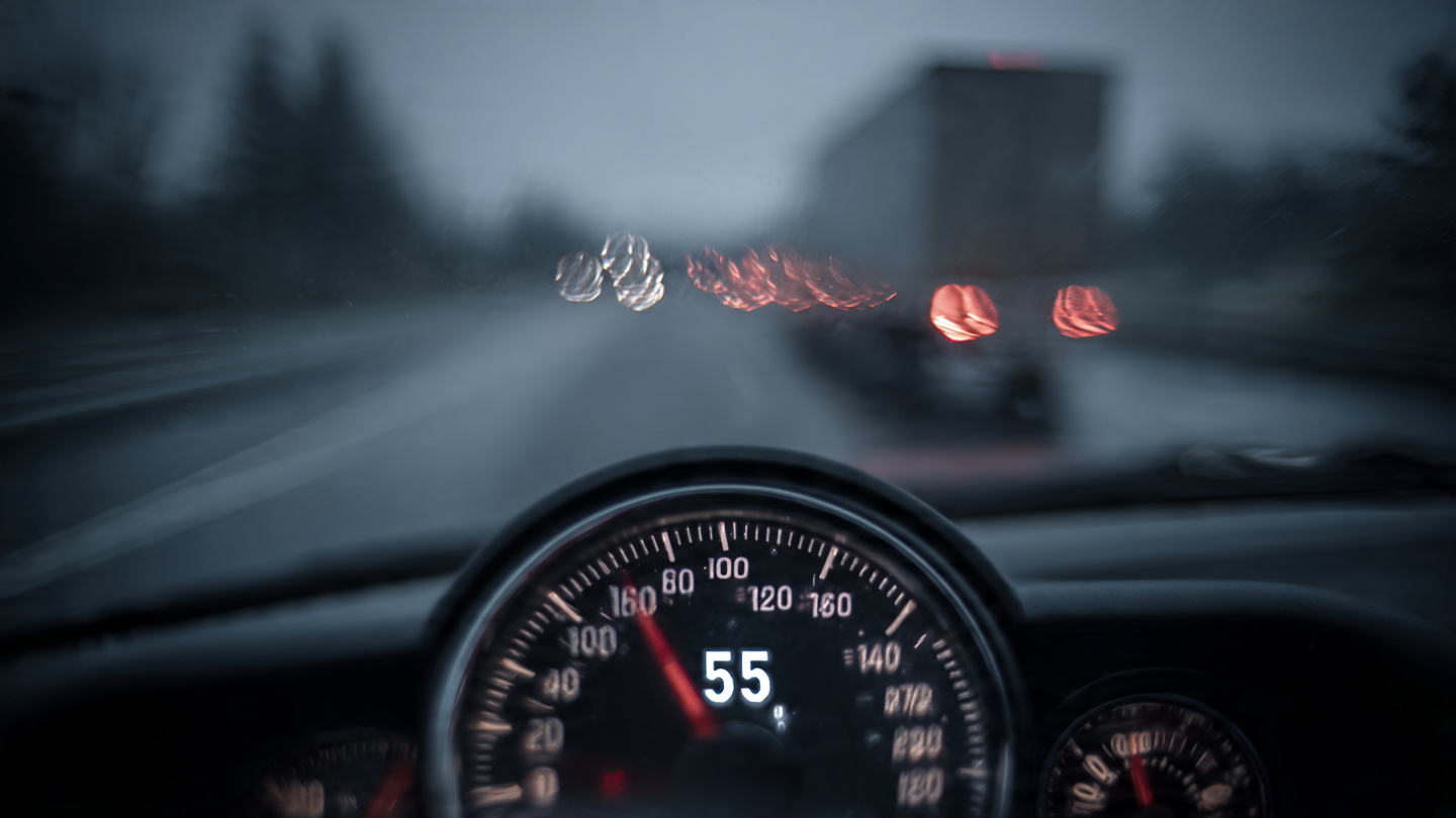 A parking lot speed limit sign juxtaposed against a highway, representing the gap between AEB test speeds and real-world crash speeds