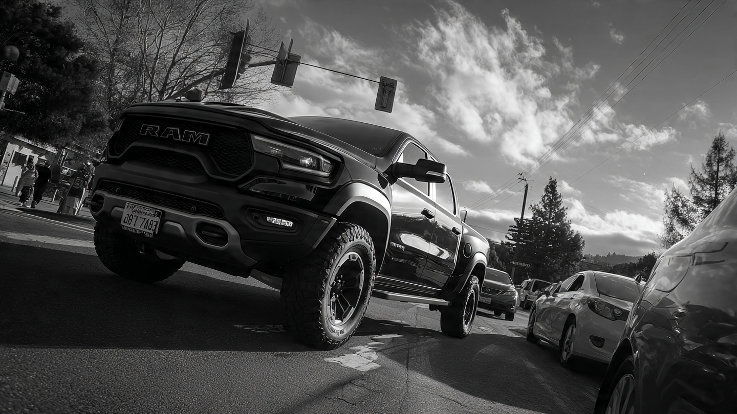 A massive pickup truck towering over a compact sedan at an intersection