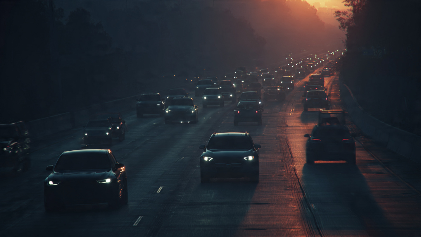 A divided highway at dusk showing modern crossovers in sharp focus alongside older vehicles fading into shadow, illustrating America's two-tier fleet safety reality