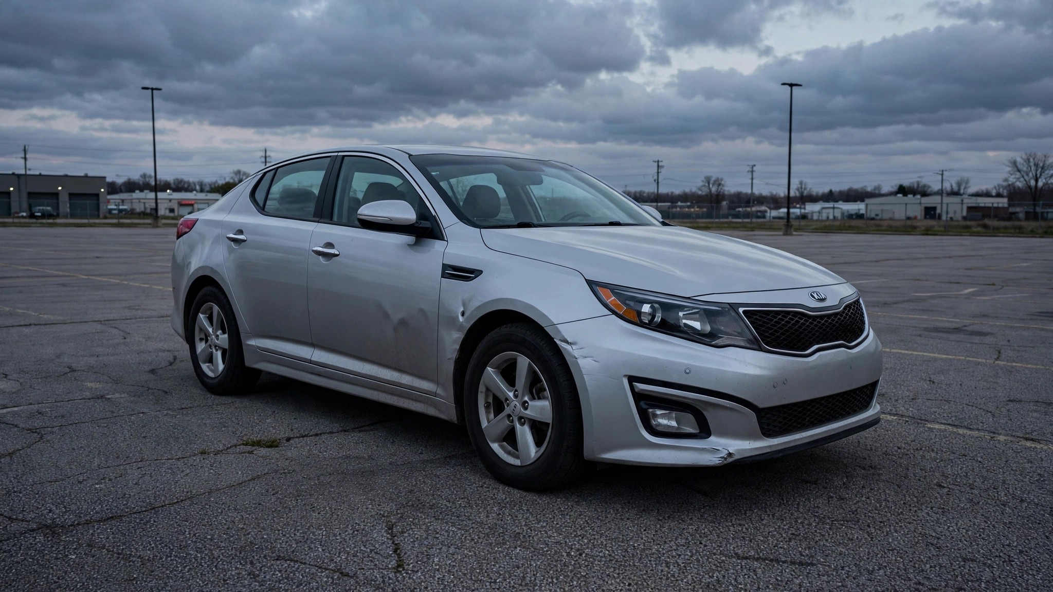 A silver Kia Optima sedan sitting alone in an empty parking lot at dusk