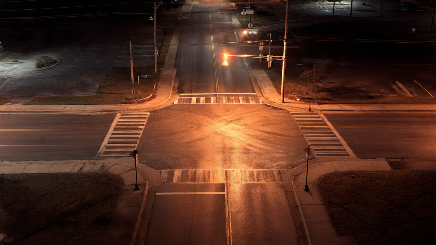 An empty suburban intersection at night with a faded crosswalk and harsh orange street lights