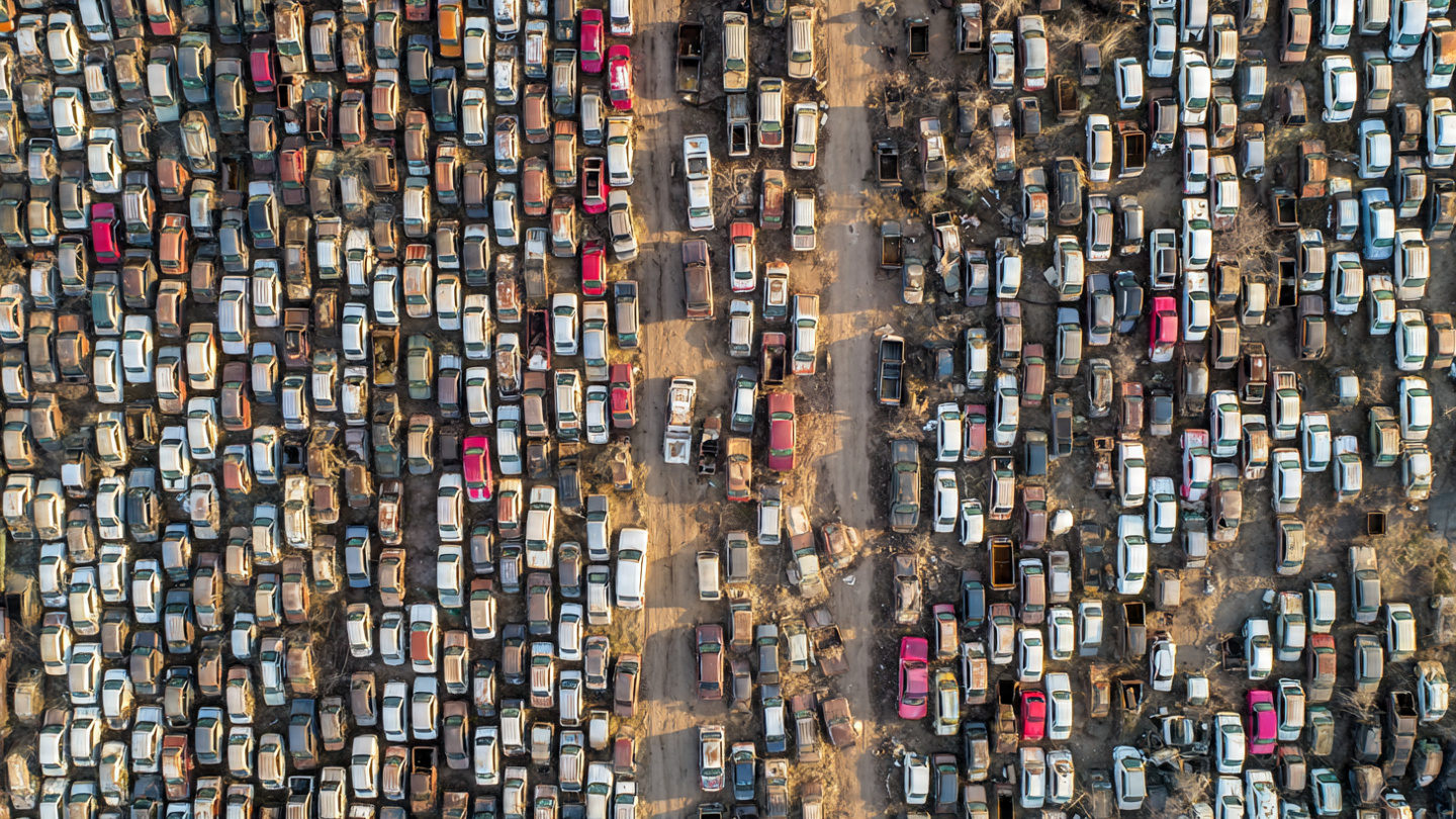 Aerial view of a vast junkyard filled with hundreds of rusting early-2000s pickup trucks